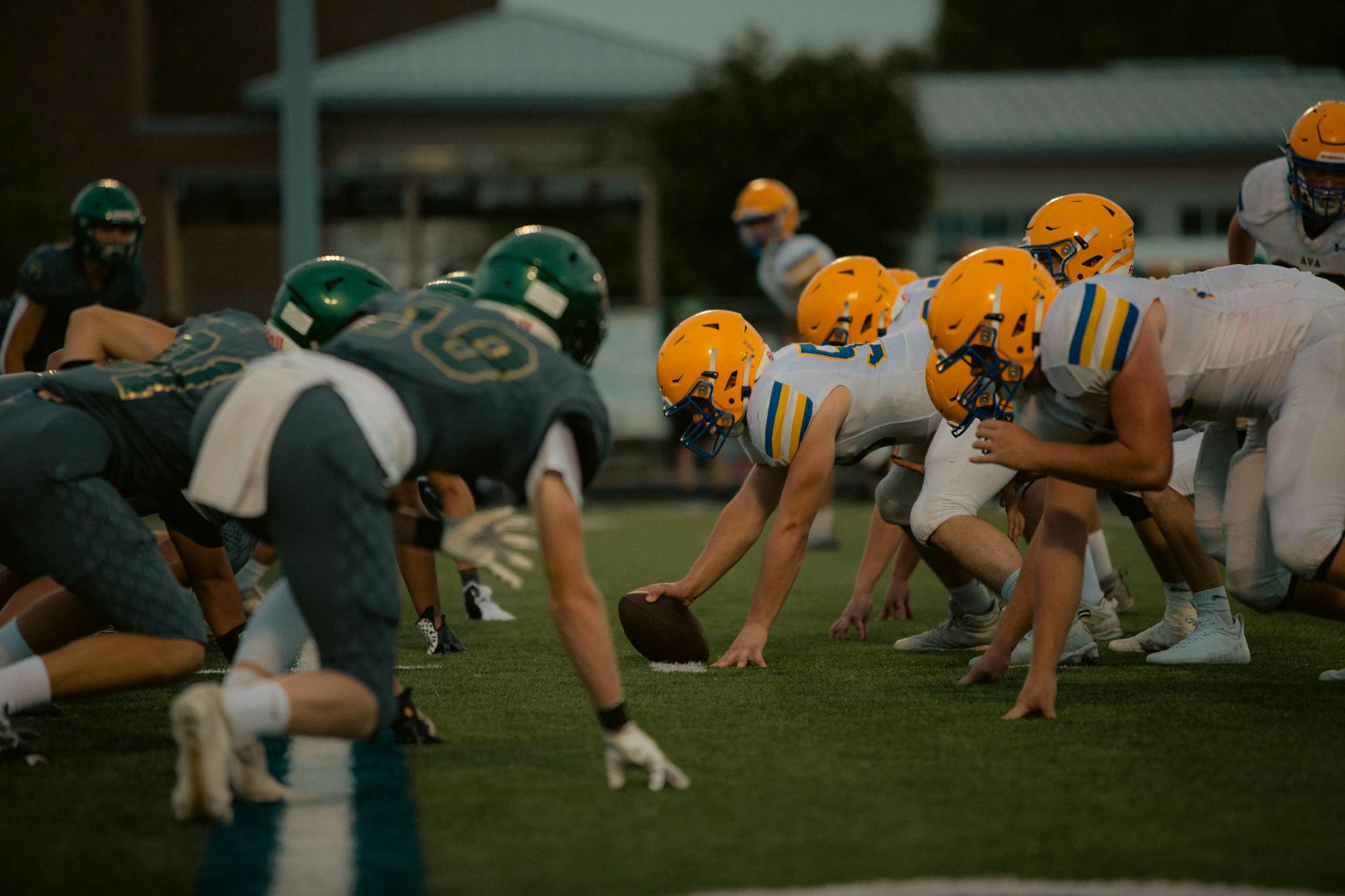 High school football teams face off at the line of scrimmage during a competitive evening game.